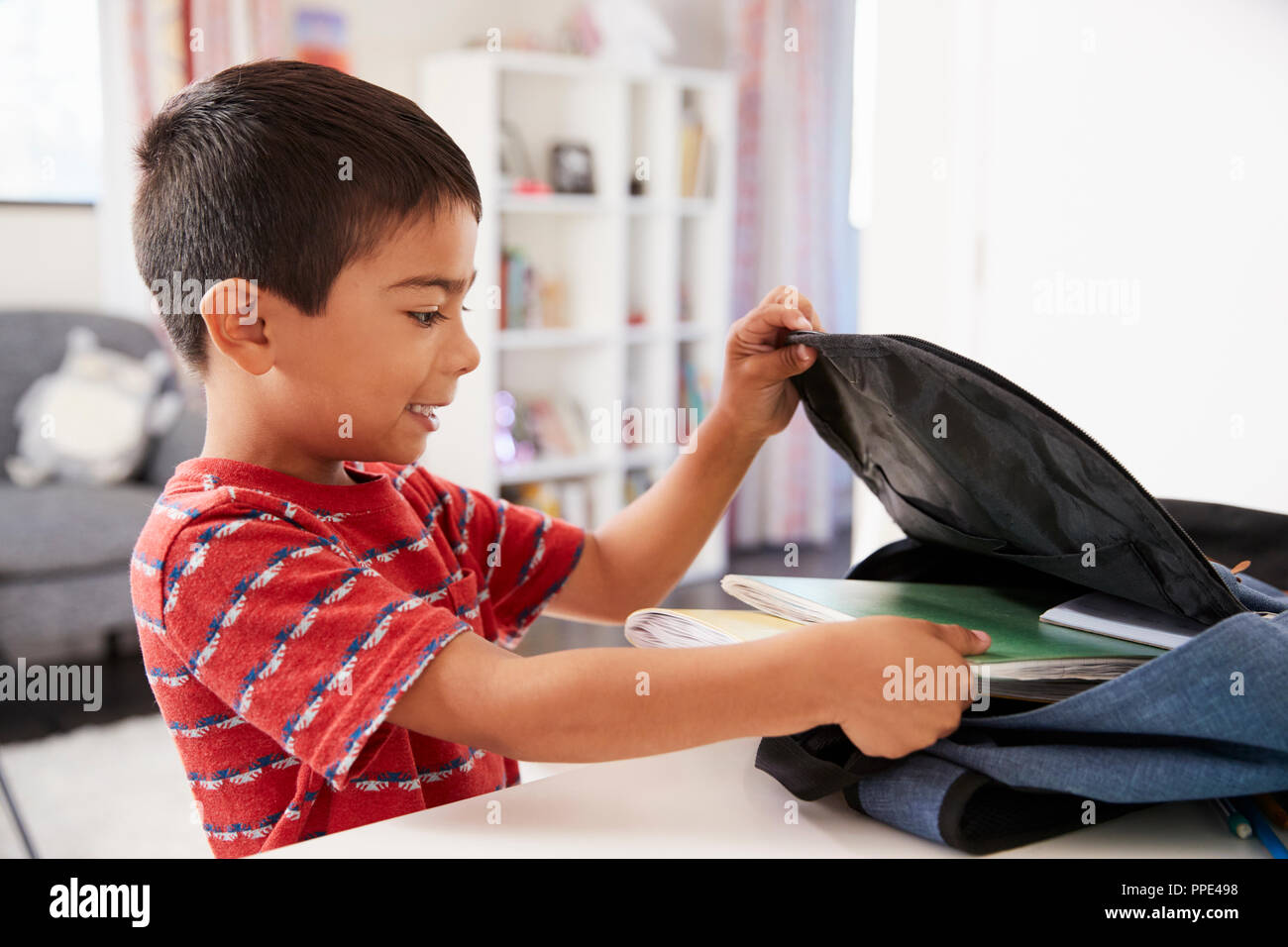Boy In Bedroom Packing Bag Ready For School Stock Photo