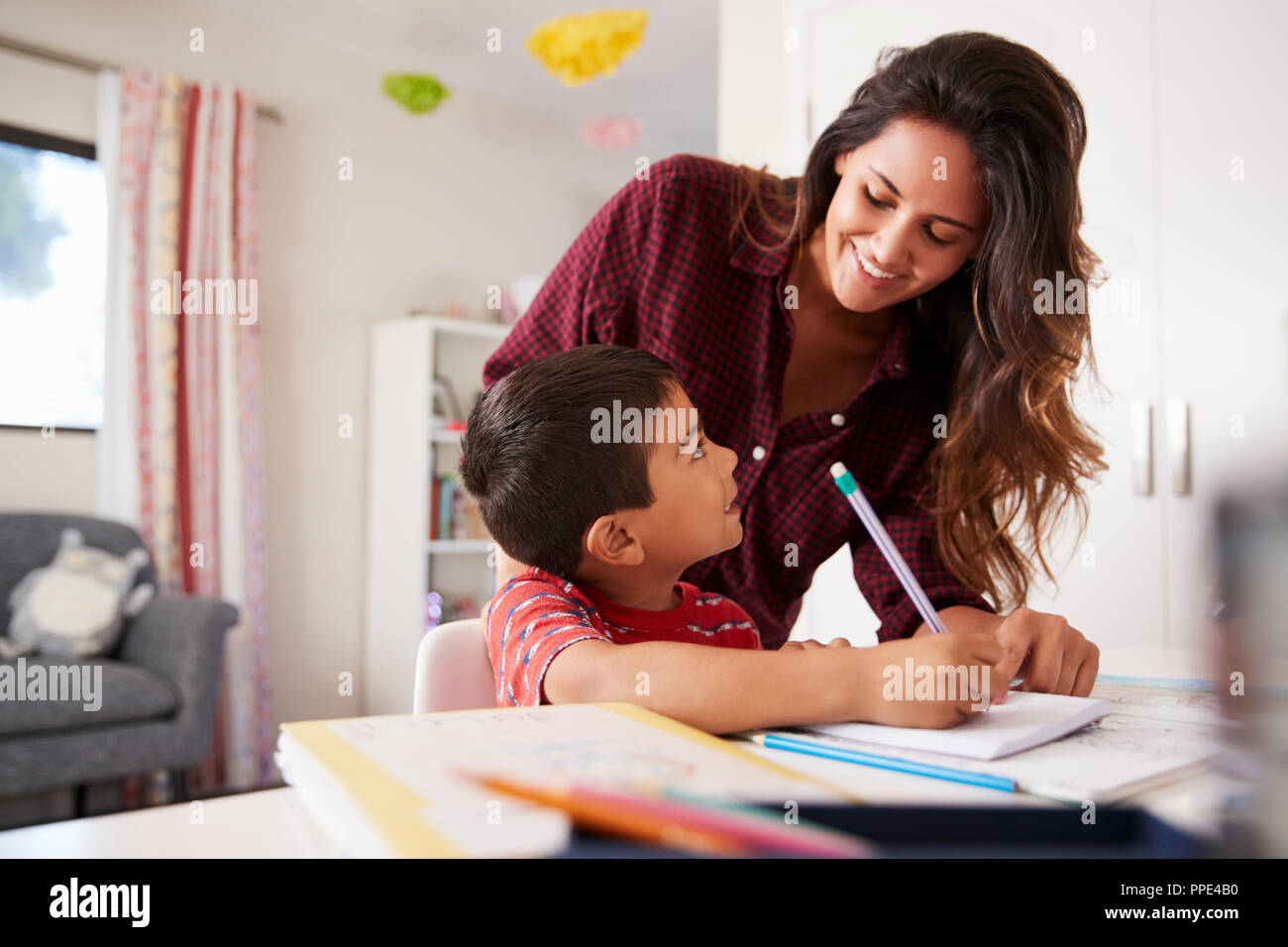 Mother Helping Son With Homework Sitting At Desk In Bedroom Stock Photo