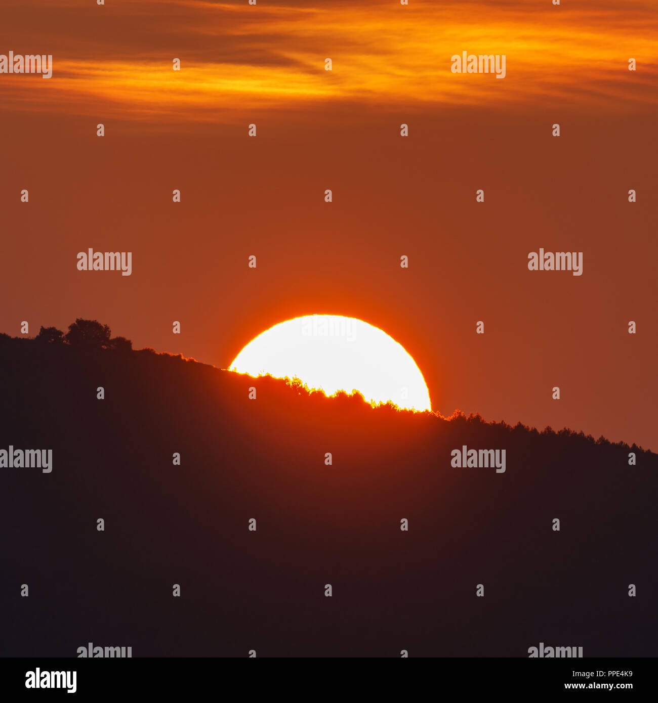 Sun behind mountain at sunrise, orange colors Stock Photo