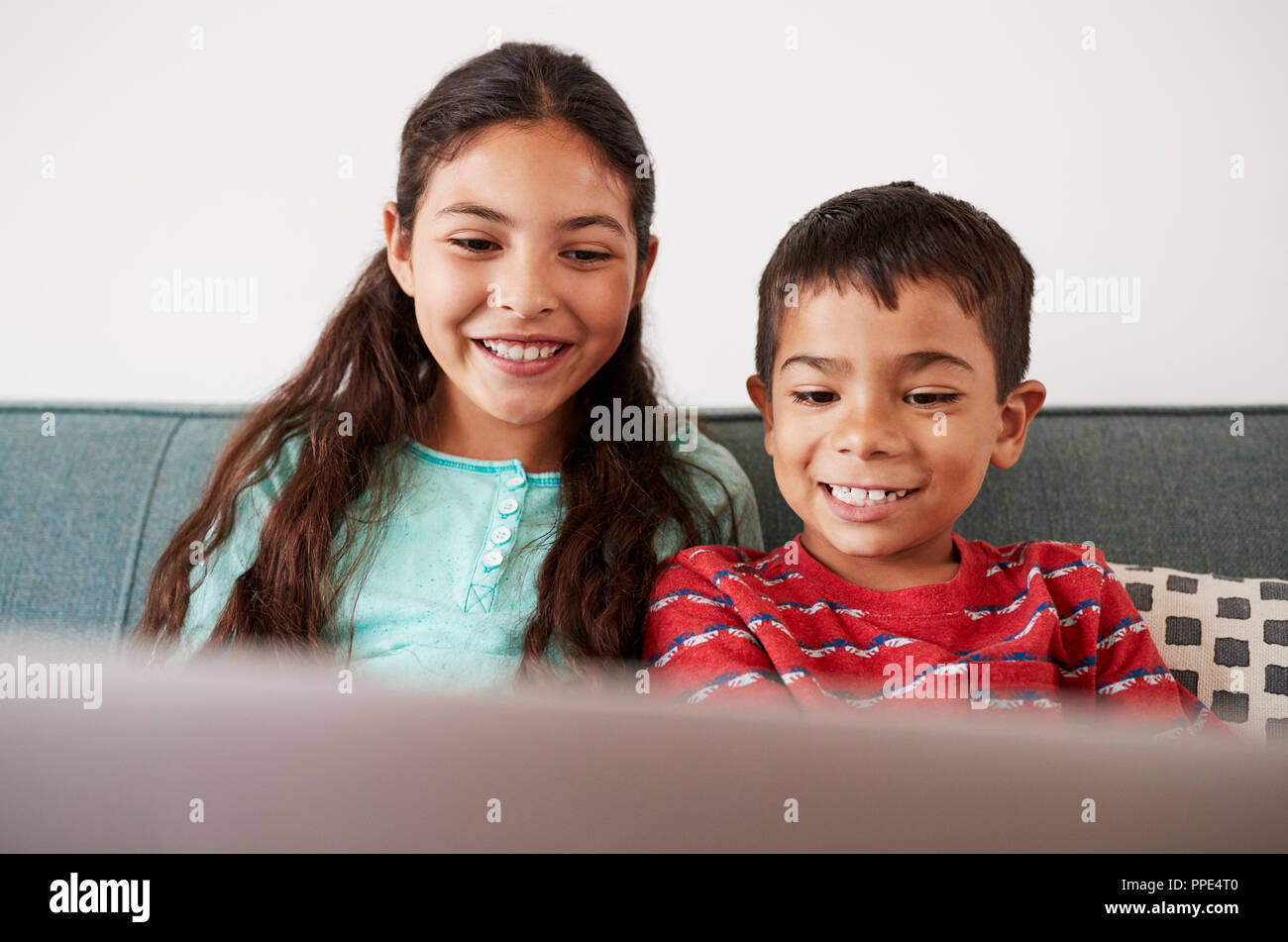 Brother And Sister Sitting On Sofa At Home Having Fun Playing On Laptop