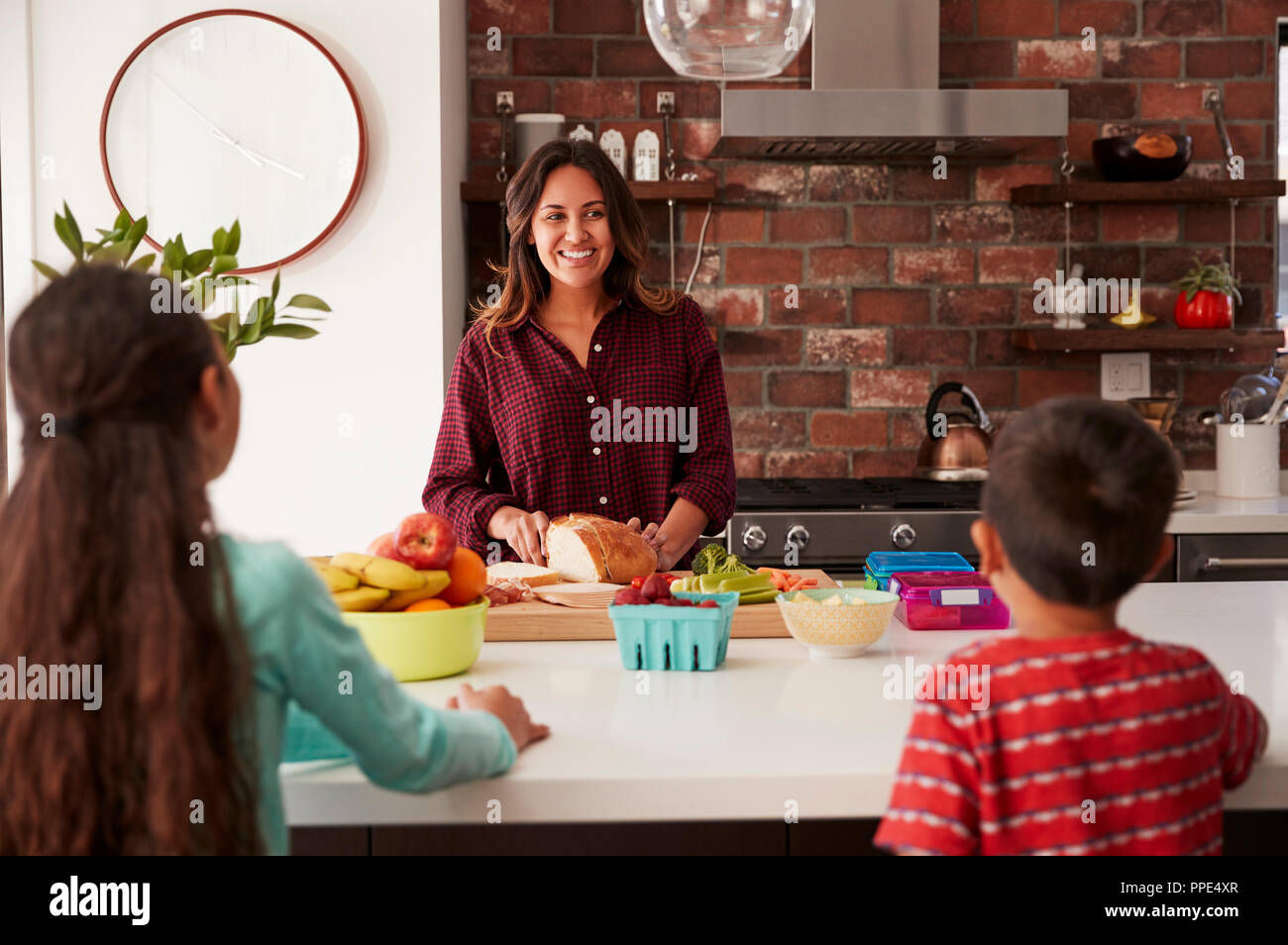 Mother Making School Lunches For Children In Kitchen At Home Stock Photo