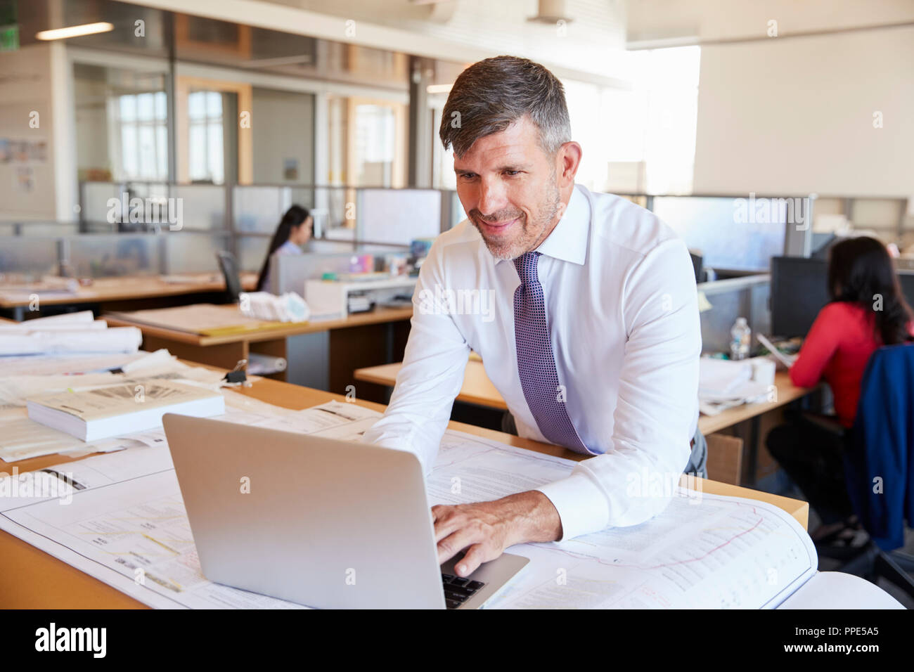 Middle aged male architect using laptop in open plan office Stock Photo