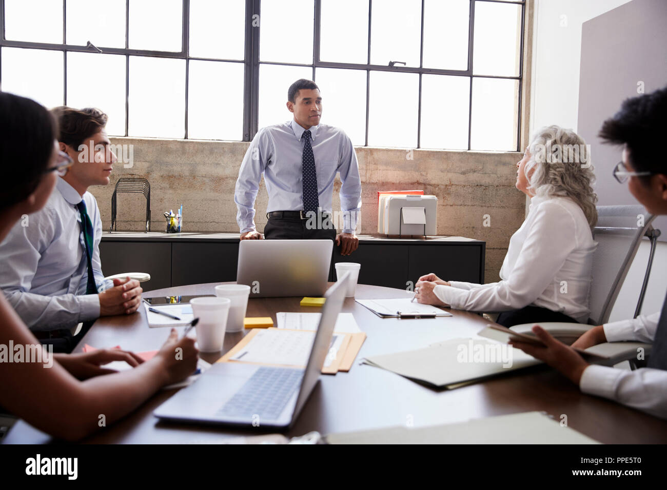 Male manager stands listening to team in brainstorm meeting Stock Photo ...