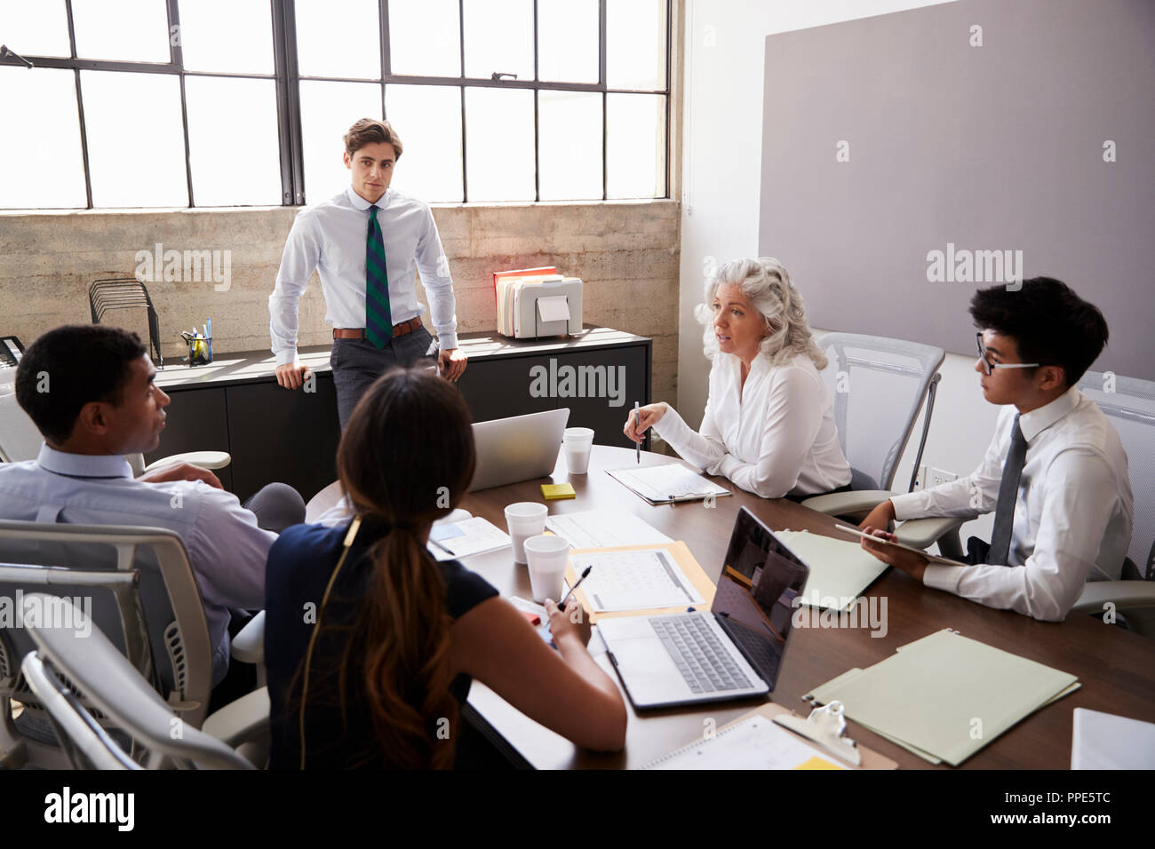 Young male manager stands listening to team at a meeting Stock Photo