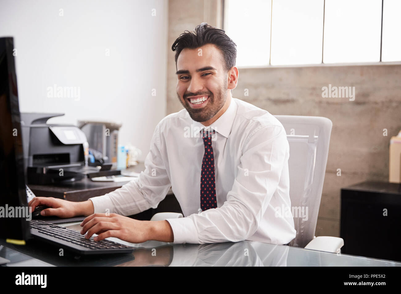 Young Hispanic businessman using computer smiling to camera Stock Photo