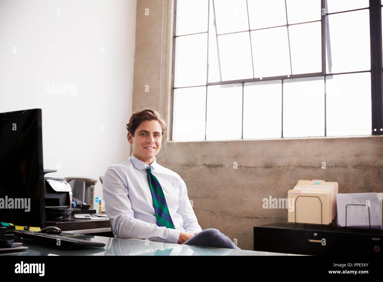 Young white businessman sitting in office smiling to camera Stock Photo