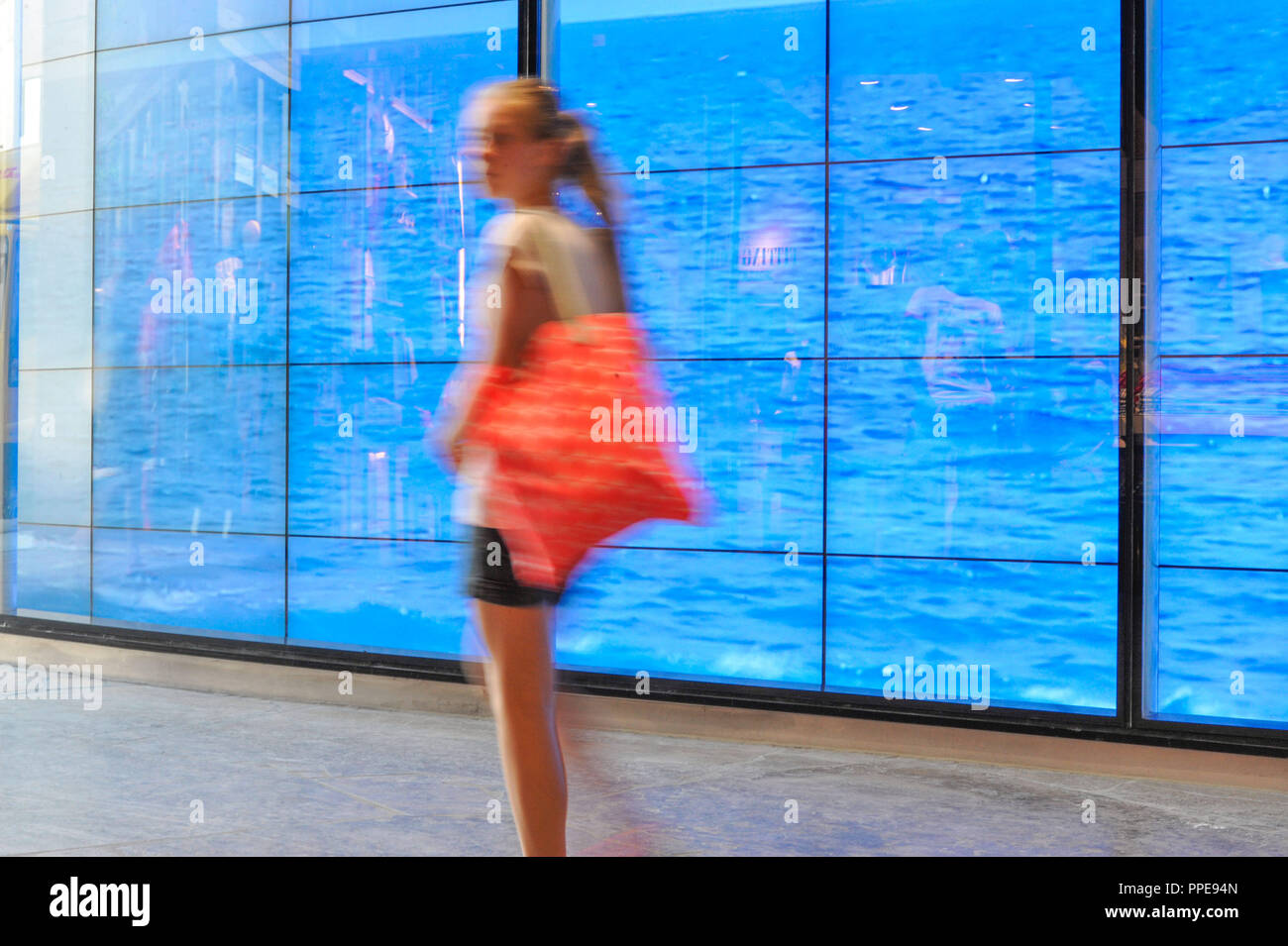 A young woman during a 'beach walk', even if only in front of a video projection of the sea in the display window of the shop Hollister in the Hofstatt in Munich. Stock Photo