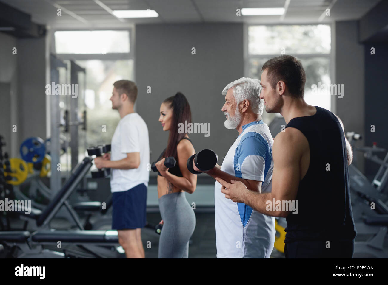 Elderly man doing exercise with dumbbell at gym with group of diverse