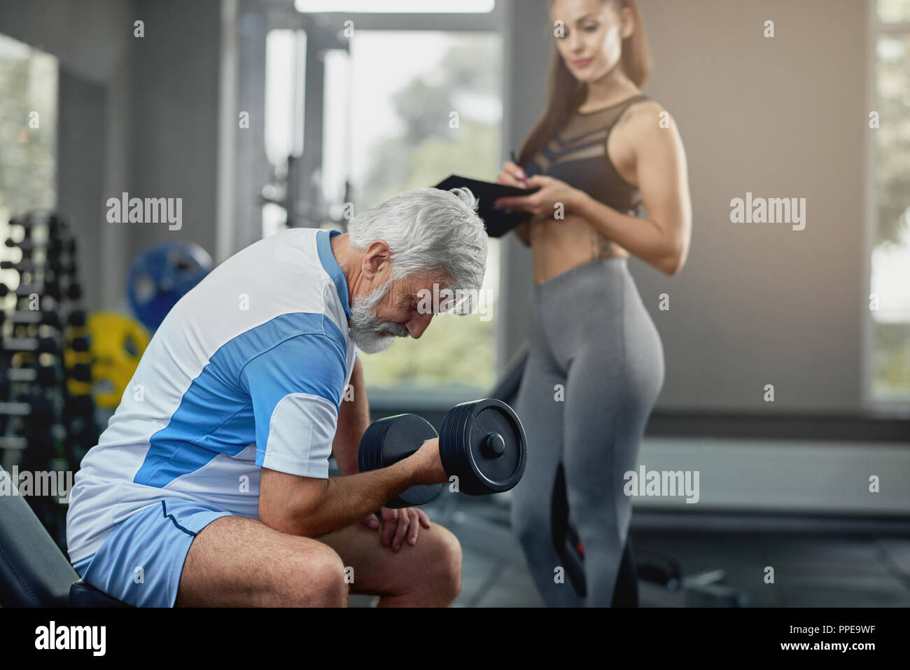 Beautiful girls with long hair is training in the gym with weights. Personal  fitness trainer is at work doing exercises for good muscles. Sport  motivation healthy lifestyle. Woman body workout. Stock Photo