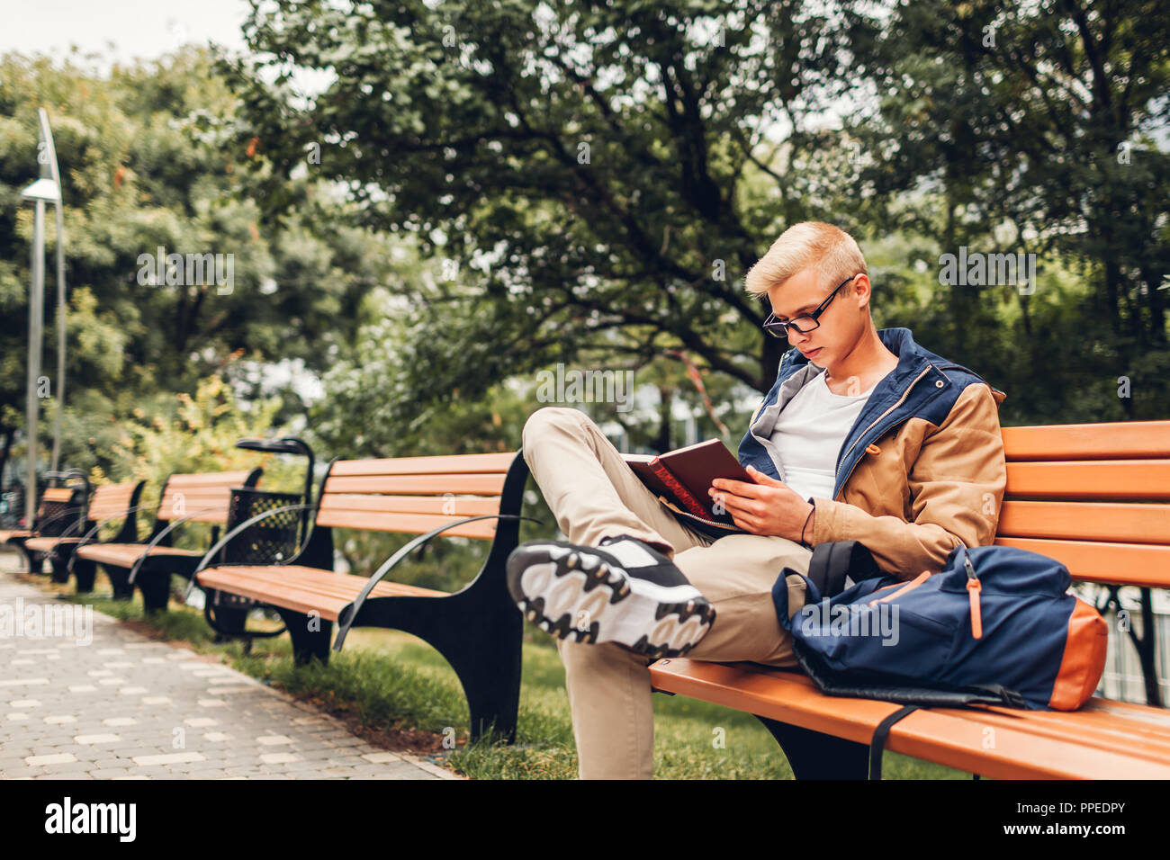 College student with backpack reading book walking in autumn park sitting  on bench. Man studying outdoors Stock Photo - Alamy
