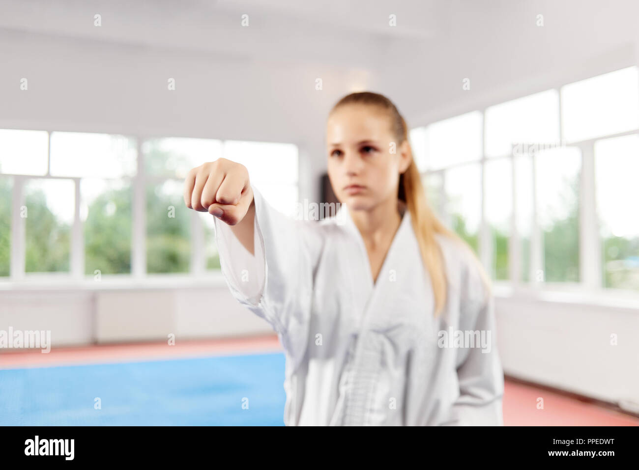 Close of woman fist throwing punch against big window at fight class. On blur background female fighter with blue eyes and braided hair seriously looking straight with clenched fist. Concept of sport. Stock Photo