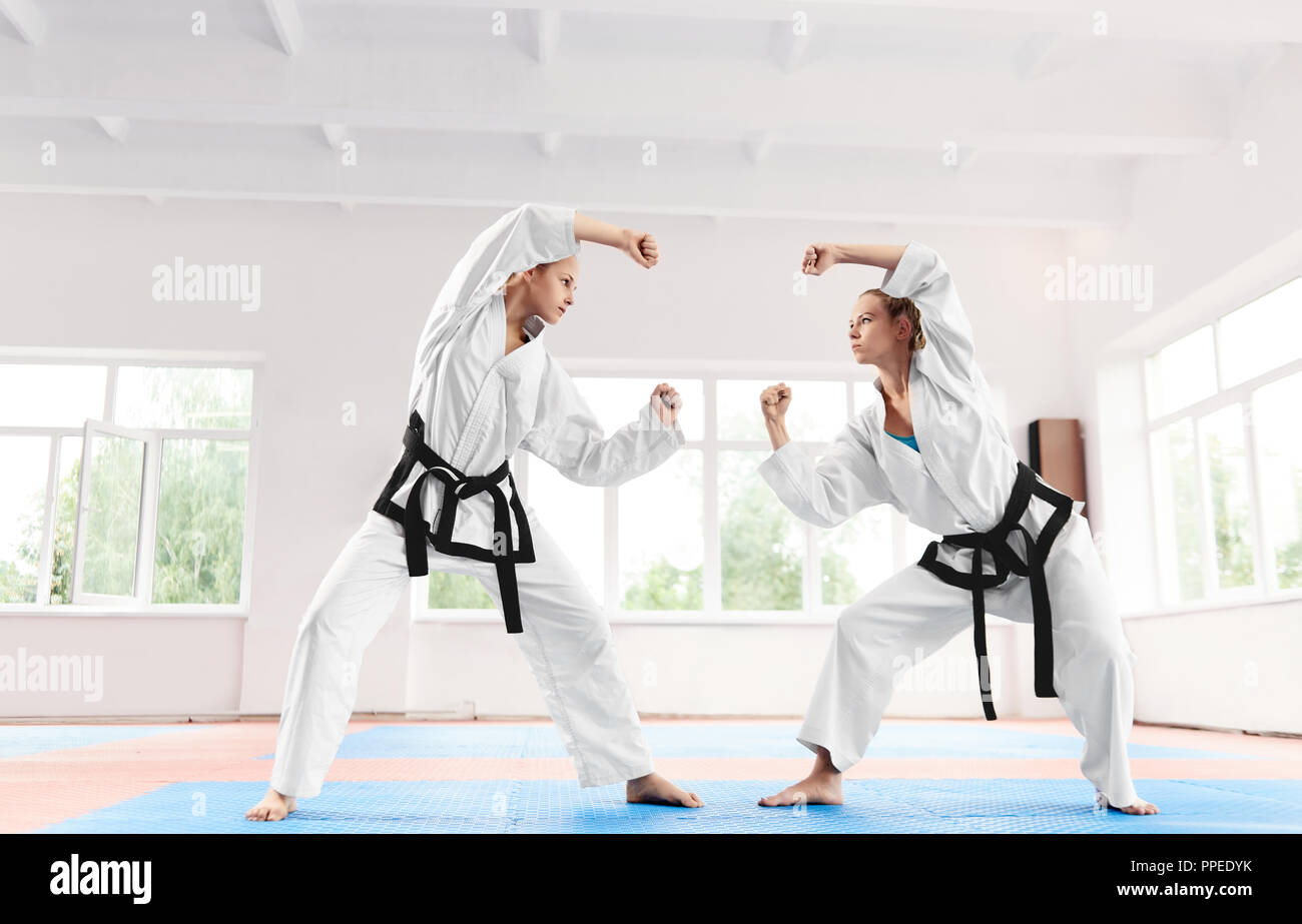 Two sporty woman fighting at karate training in martial arts school. Strong women wearing in white kimono and black belts doing competitions among themselves. Healthy lifestyle and sports concept. Stock Photo