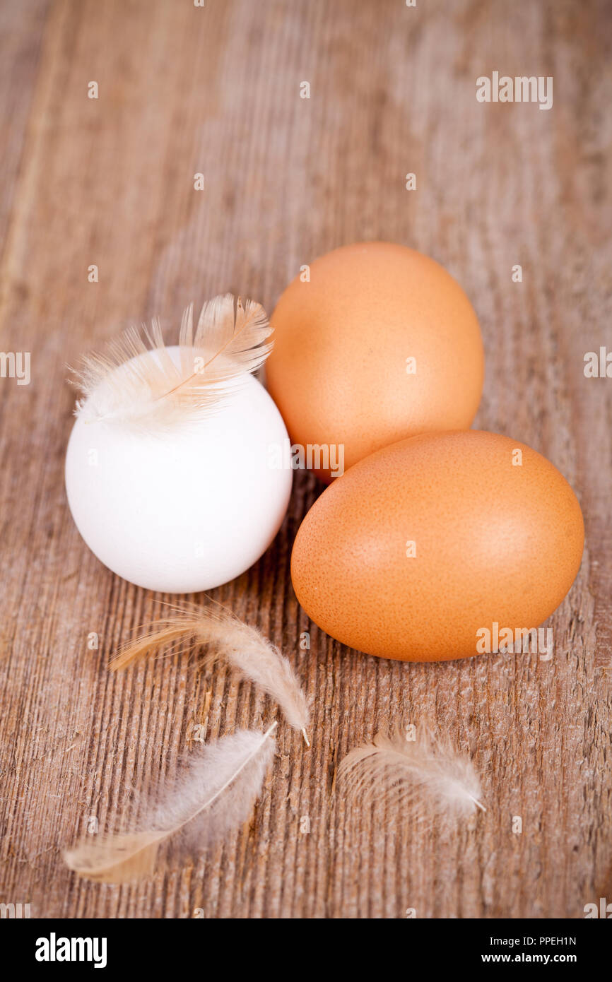 three eggs and feathers on rustic wooden table Stock Photo