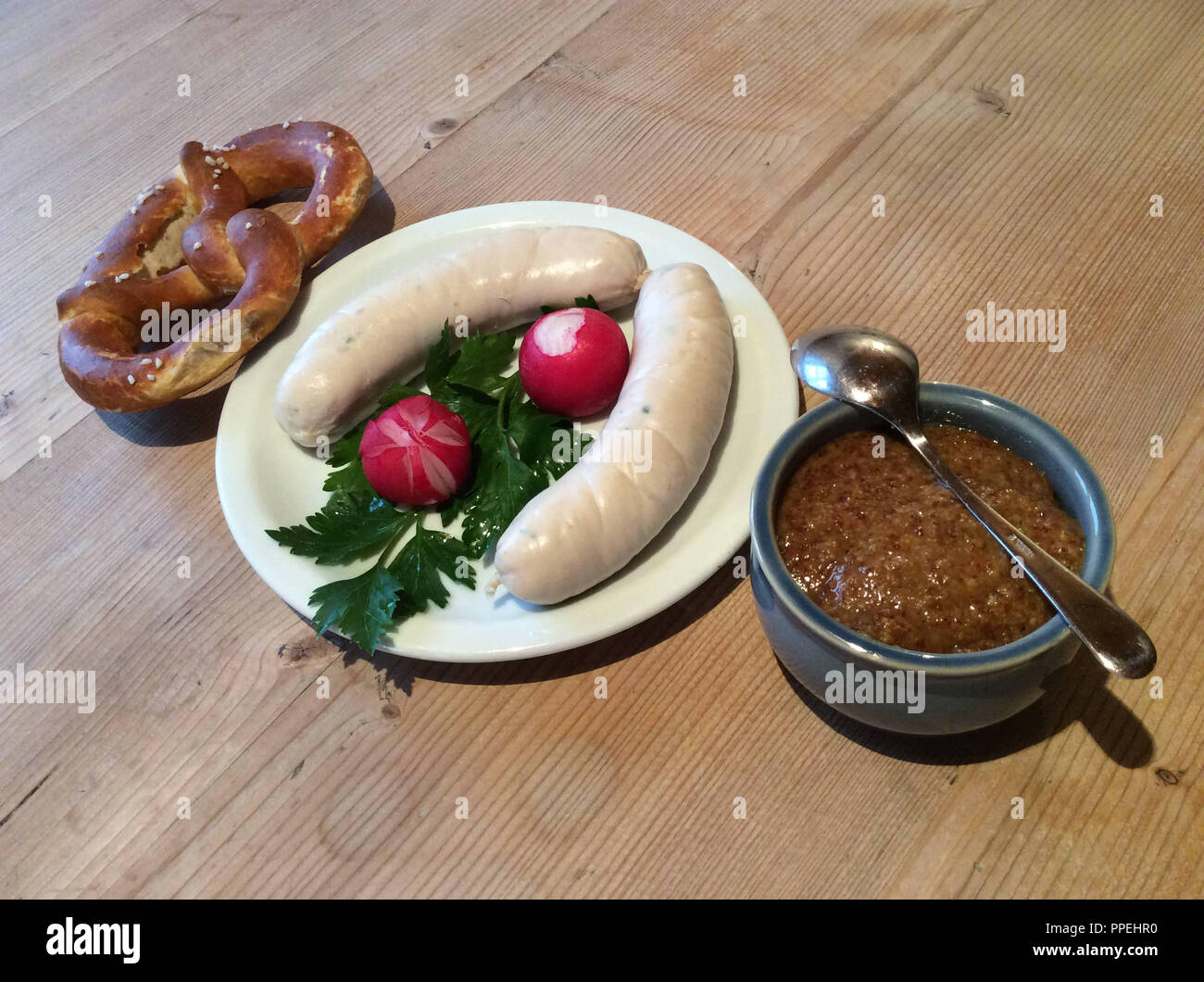 Weisswurst snack or breakfast with pretzel, rolls, parsley and mustard on a rustic wooden table. Stock Photo