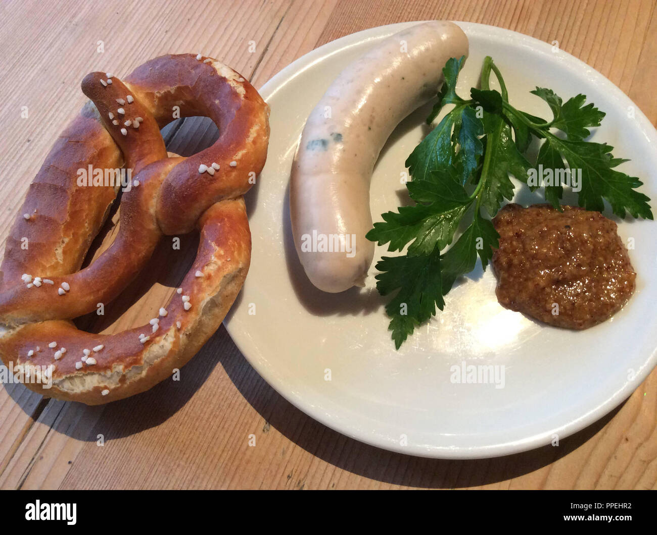 Weisswurst snack or breakfast with pretzel, parsley and mustard on a rustic wooden table. Stock Photo