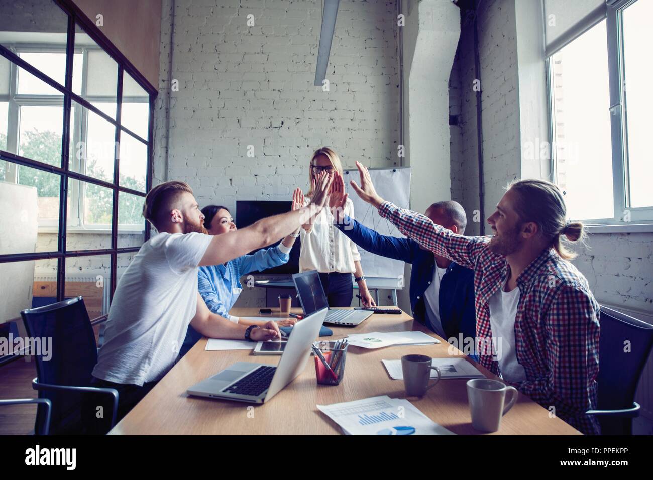 Happy successful multiracial business team giving a high fives gesture as they laugh and cheer their success. Stock Photo