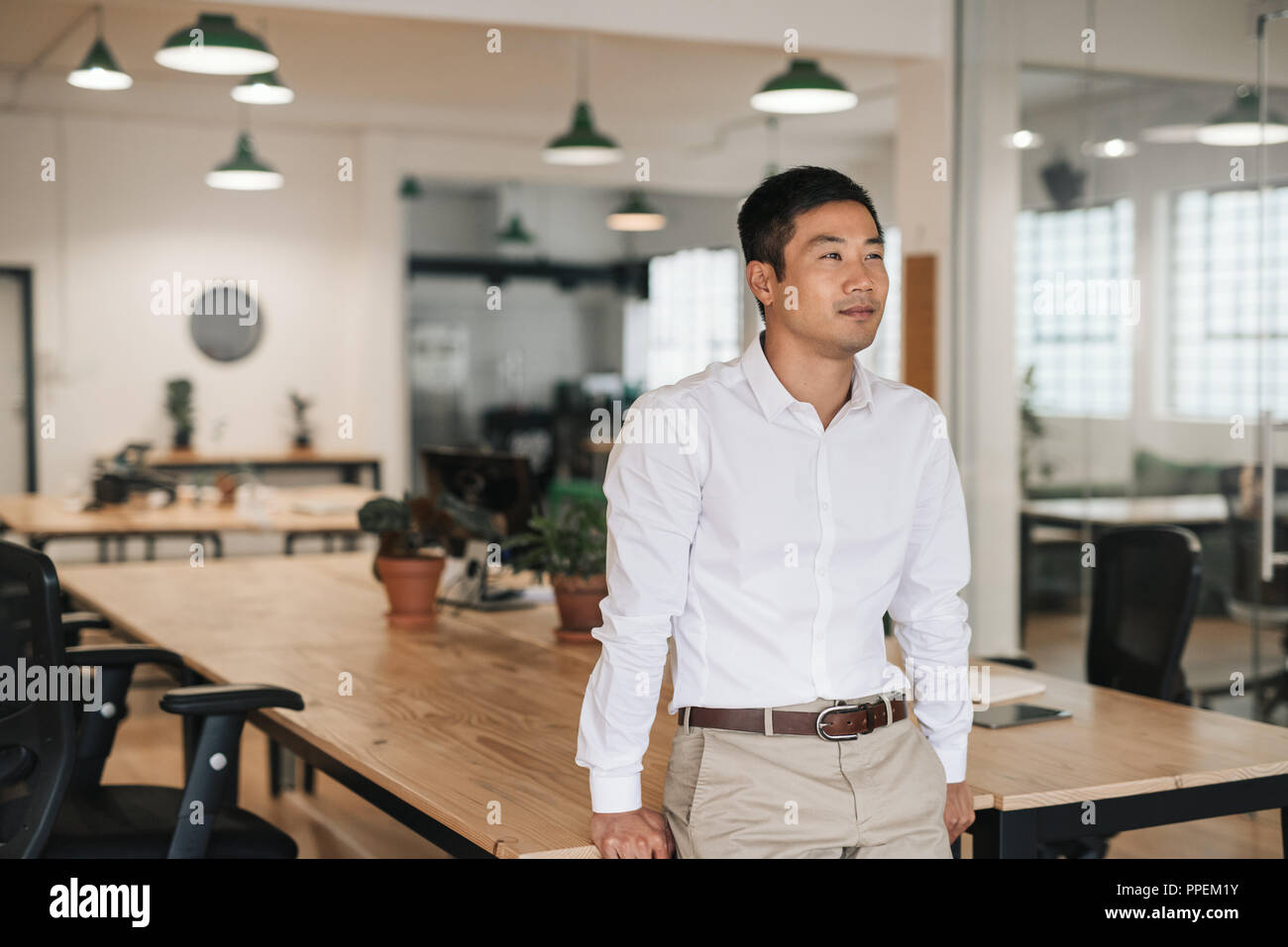 Young Asian businessman standing in an office deep in thought Stock Photo