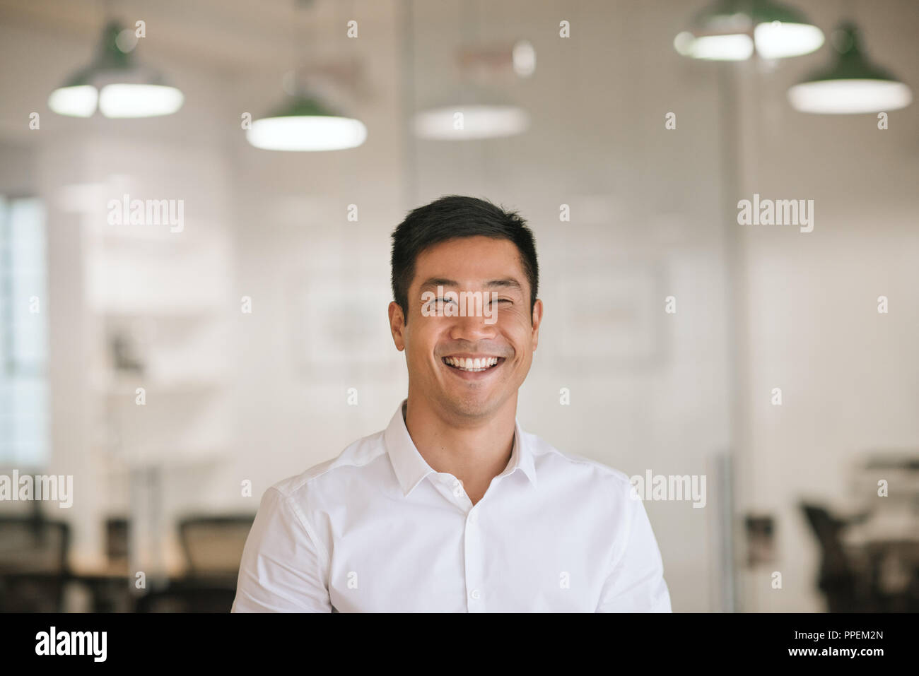 Young Asian businessman laughing while standing in a modern office Stock Photo