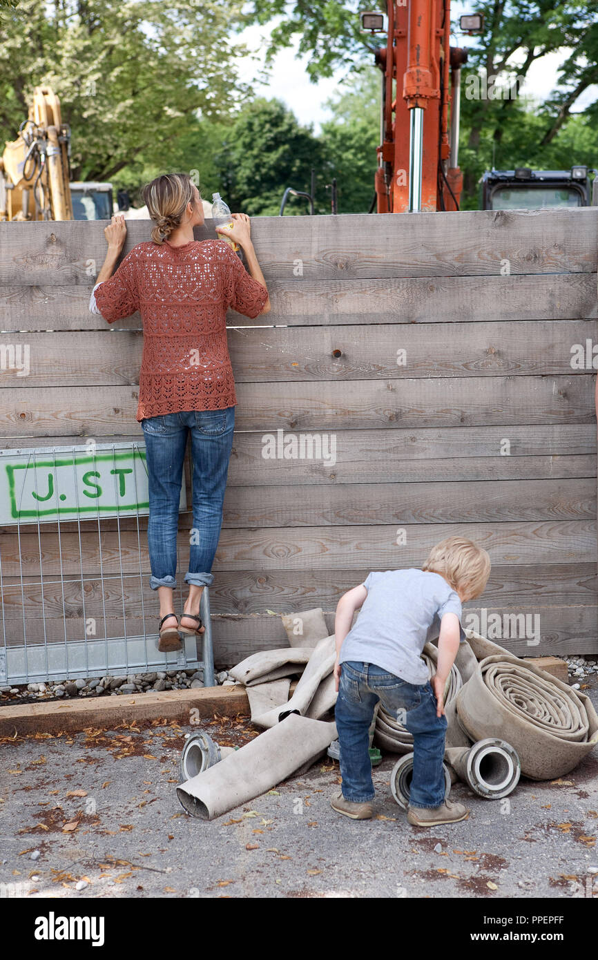 A woman climbs up a wooden fence to take a look at a construction site in Munich, Germany Stock Photo