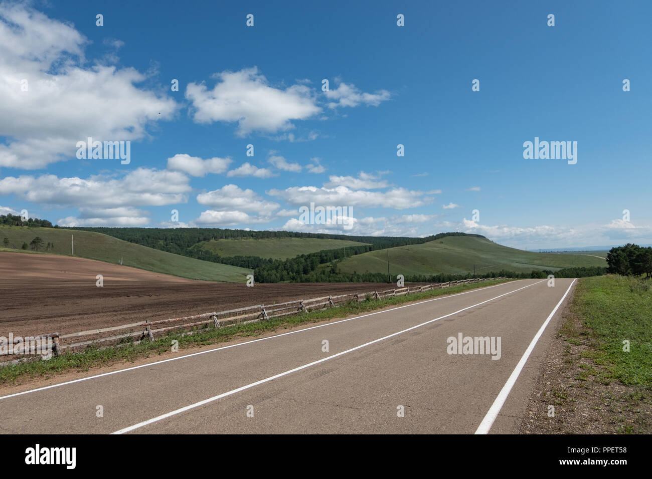 An asphalt road with white markings stretching into the distance, among ...