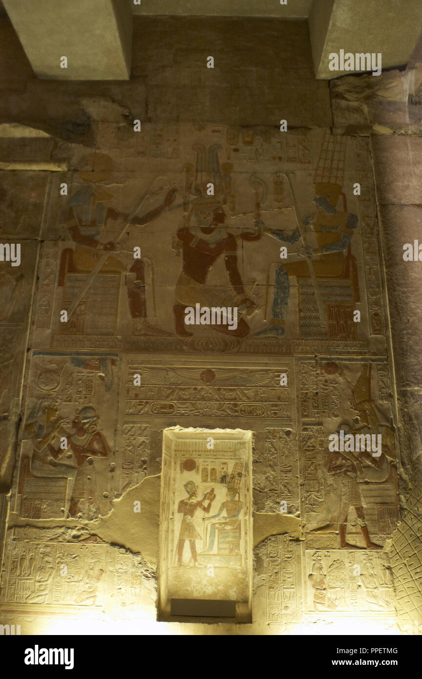Egypt. Abydos. Temple of Seti I. New Kingdom. 19th Dynasty. Relief with original polychrome, The Second Hypostyle Hall. The Pharaoh Seti I kneeling while he receives emblems from god Amun (wearing two vertical plumes on his head). God Khnum to the left (head of a ram). 1292-1189 BC. Stock Photo