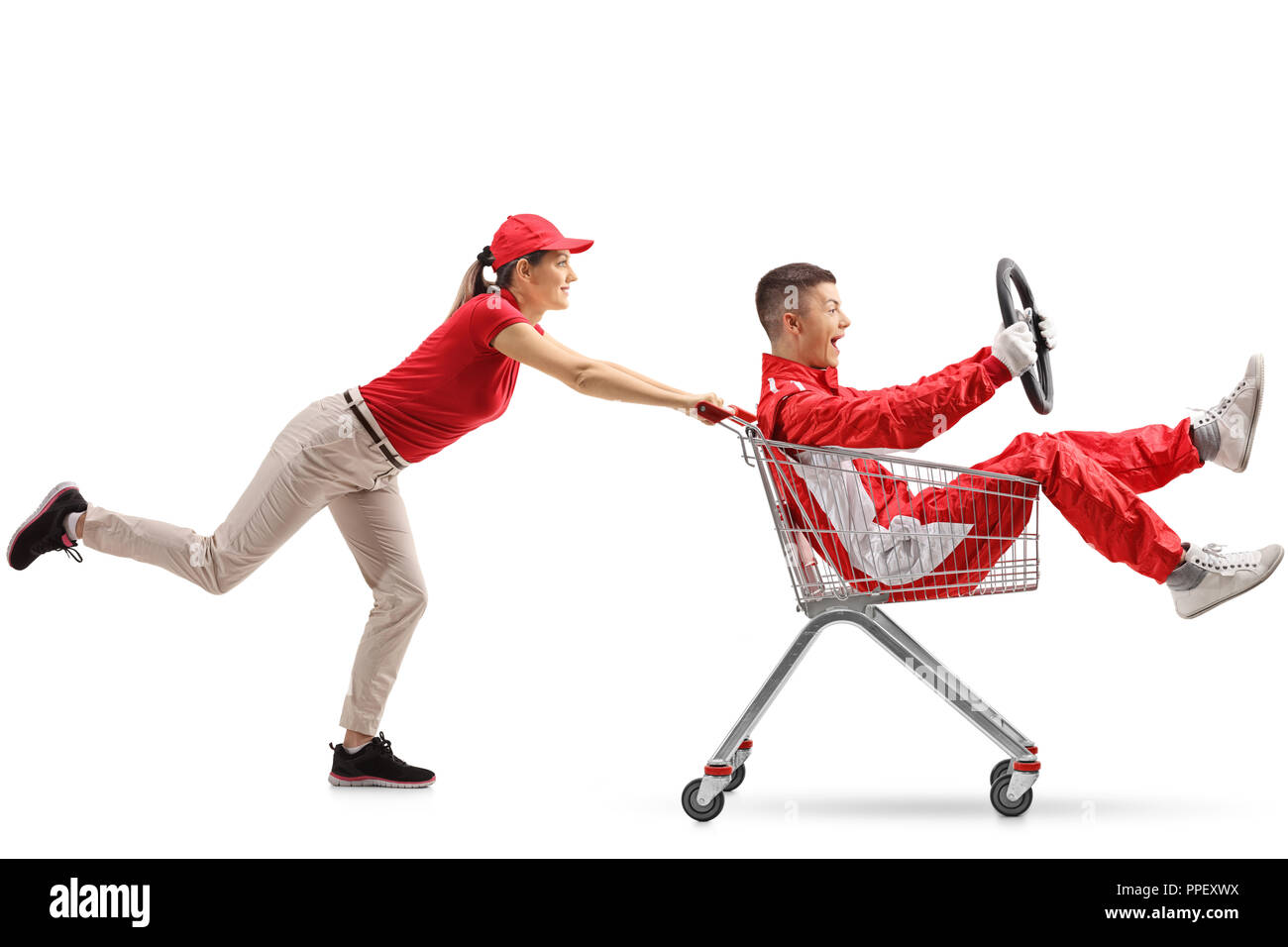 Female pushing a shopping cart with a teenage boy in a racing suit holding a steering wheel isolated on white background Stock Photo