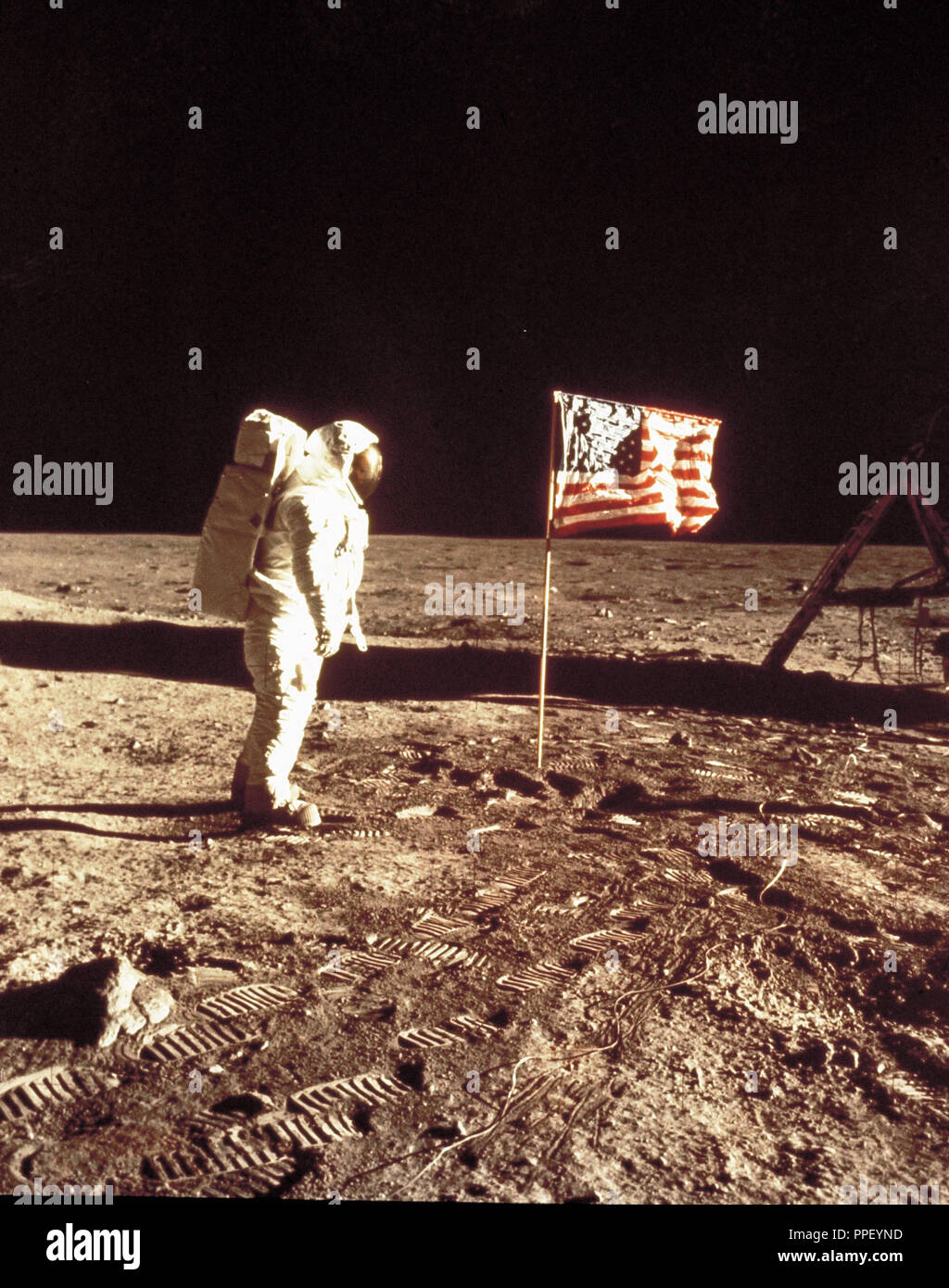 Astronaut Edward Aldrin poses beside deployed US flag. The lunar module is on the left. The astronaut's footprints are clearly visible in the foreground. Stock Photo