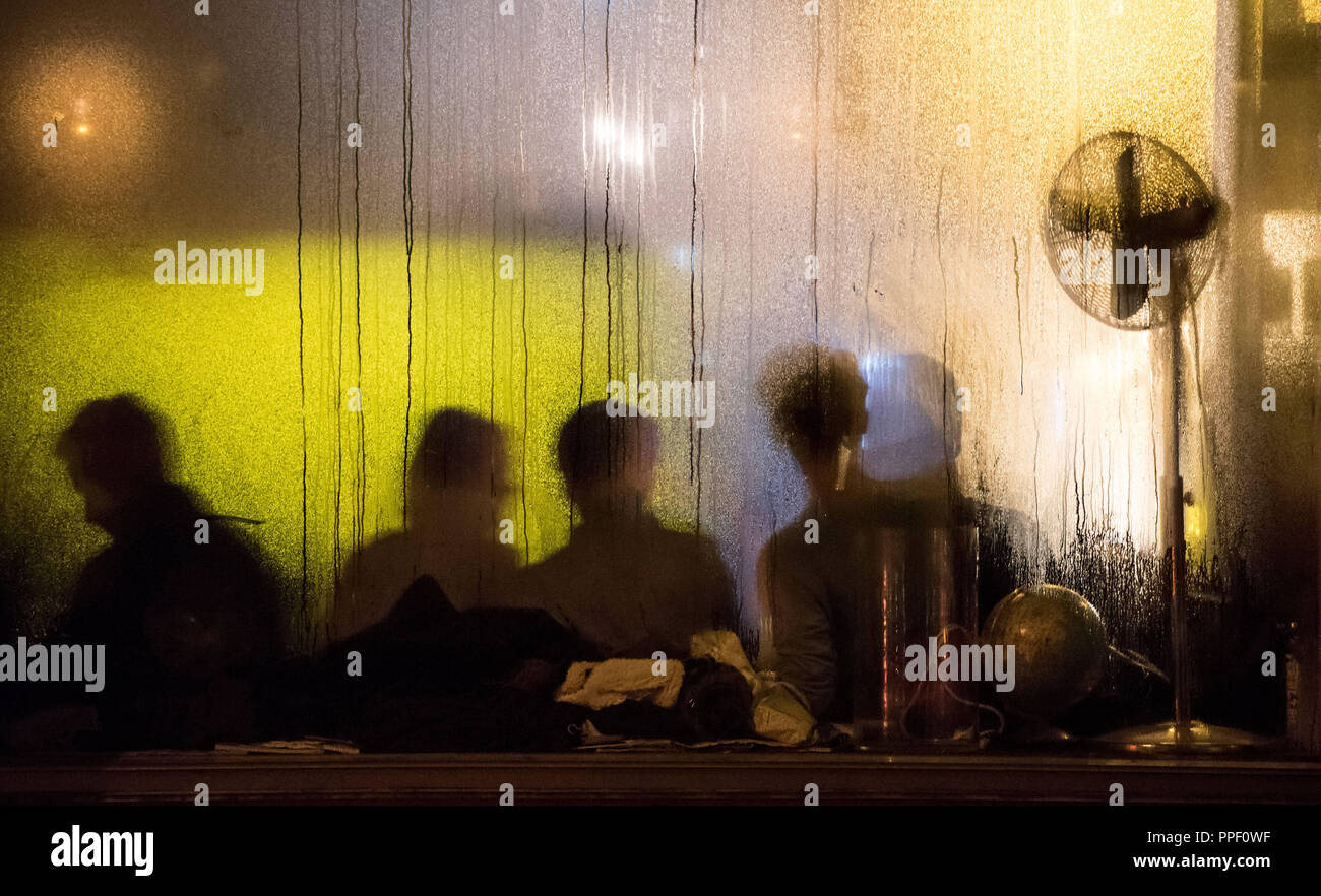 Silhouettes of guests of a bar in the Muellerstrasse in Munich can be seen behind the glass covered with water droplets. Stock Photo