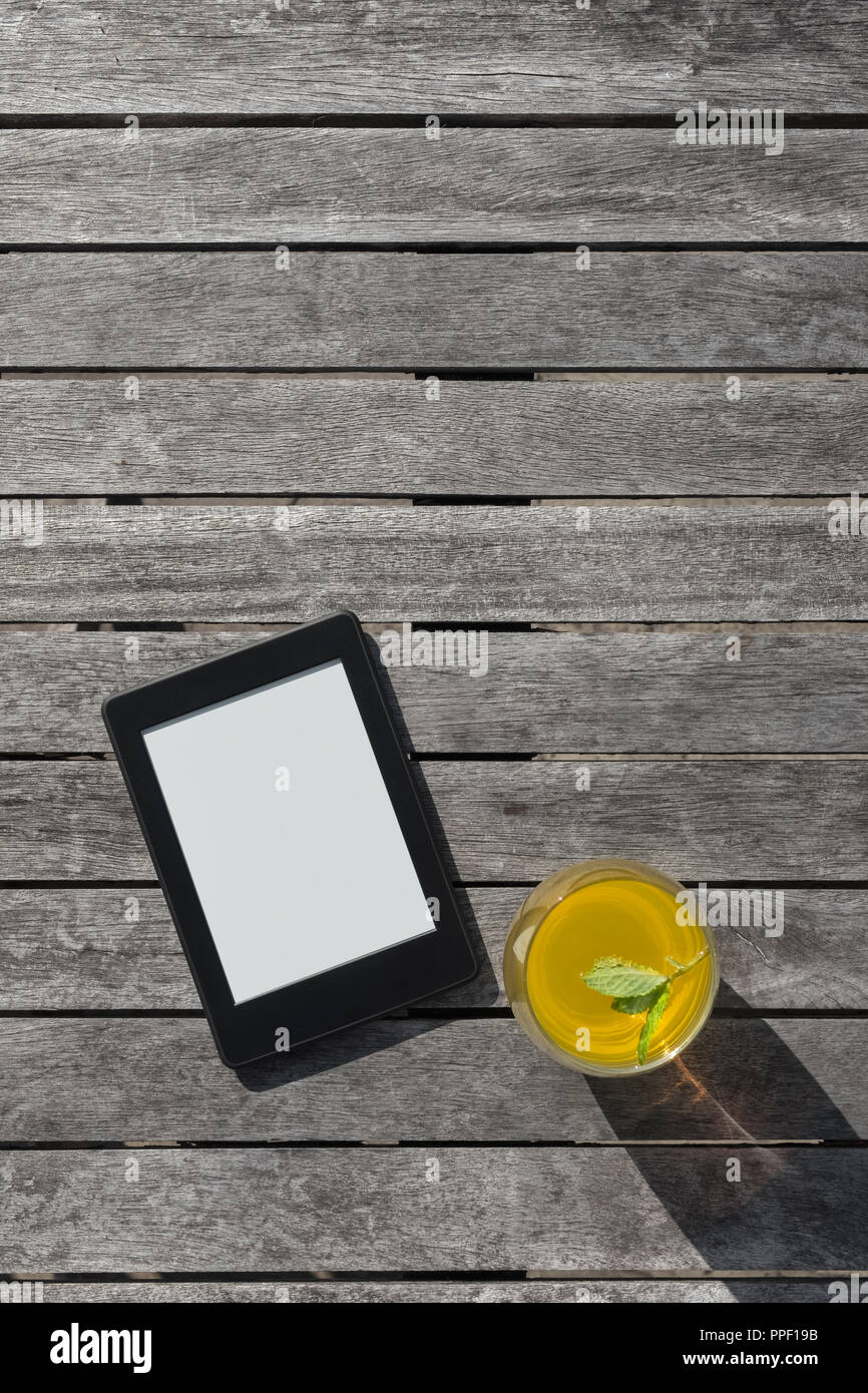 E-reader and a glass of fruit drink on a wooden table. Stock Photo