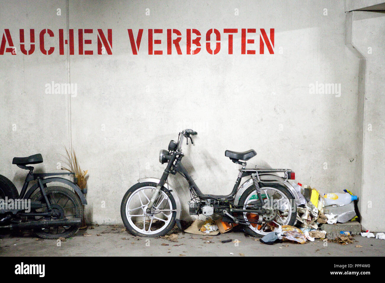 Garbage and broken bikes in the underground garage of a housing complex at the Carl-Orff-Bogen. On the wall the words 'No smoking'. Stock Photo