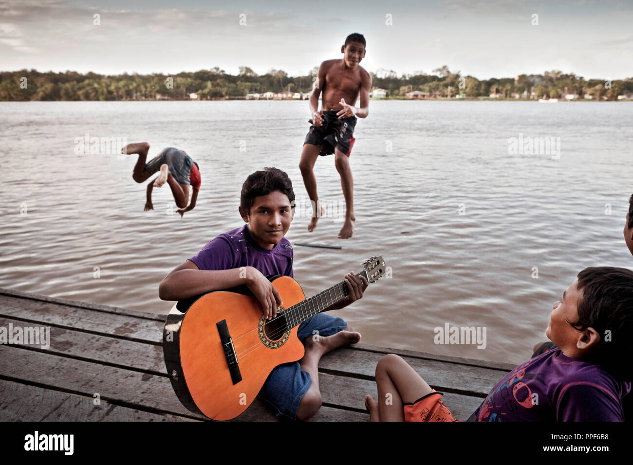 Teenagers spend with guitar playing the evening on a jetty at the shore of a creek from the Amazon in Vila Progresso Brazil. Stock Photo