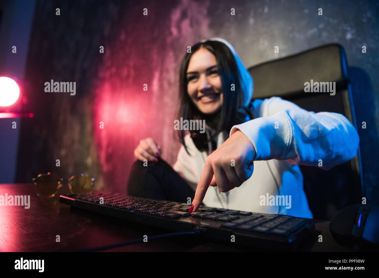 Woman in the hood sitting and working at laptop as hacker. Running malware program on computer in the internet with malevolent smile on her face. Stock Photo