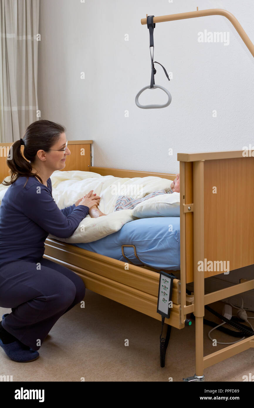 Woman at the nursing bed of her terminally ill grandmother, holding her hand and talking to her. Concept of dying at home or in a hospice. Stock Photo