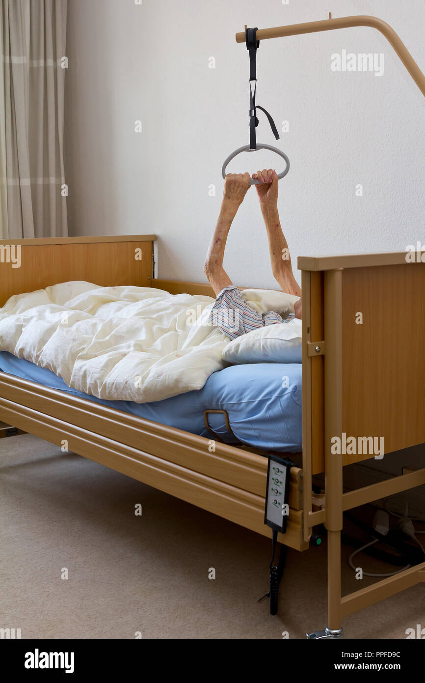 Old woman with a terminal illness trying to pull herself up with her extremely thin and weak arms on the gallow of the nursing bed in her hospice room Stock Photo
