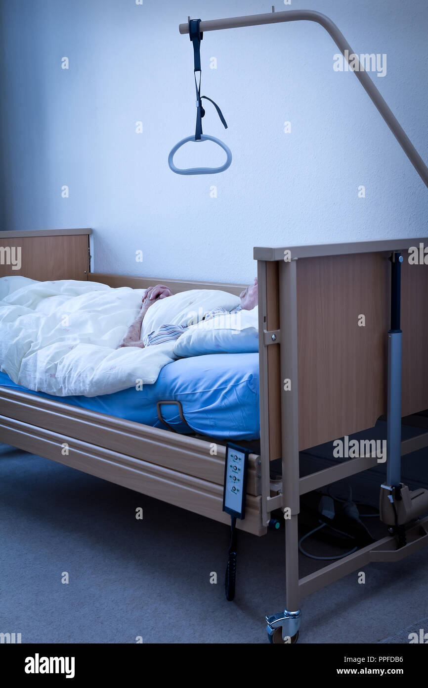 Dead person with extremly thin arms and joined hands in a nursing bed at home or in a hospice room, conept of death, blue filter effect Stock Photo