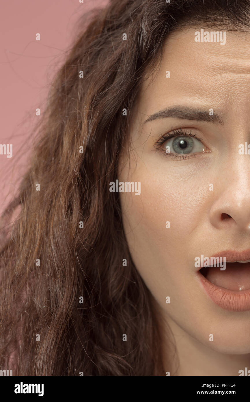Why is that. Beautiful female half face portrait isolated on trendy pink studio backgroud. Young emotional frustrated and bewildered woman. Human emotions, facial expression concept. Stock Photo