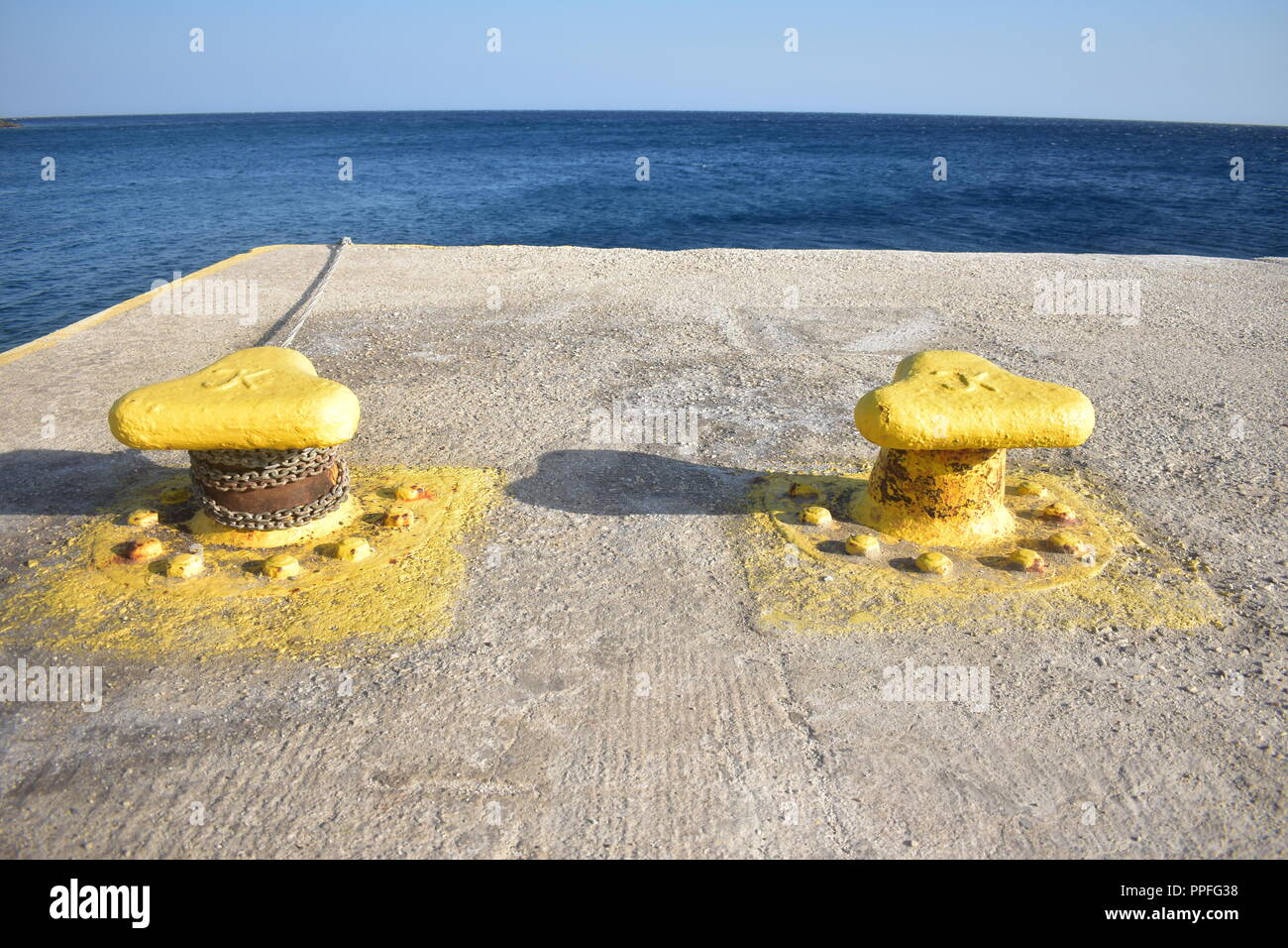 Greece, the charming, remote island of Sikinos.  Two metal yellow painted bollards at the dock of the bay, at the edge of the sea. Stock Photo