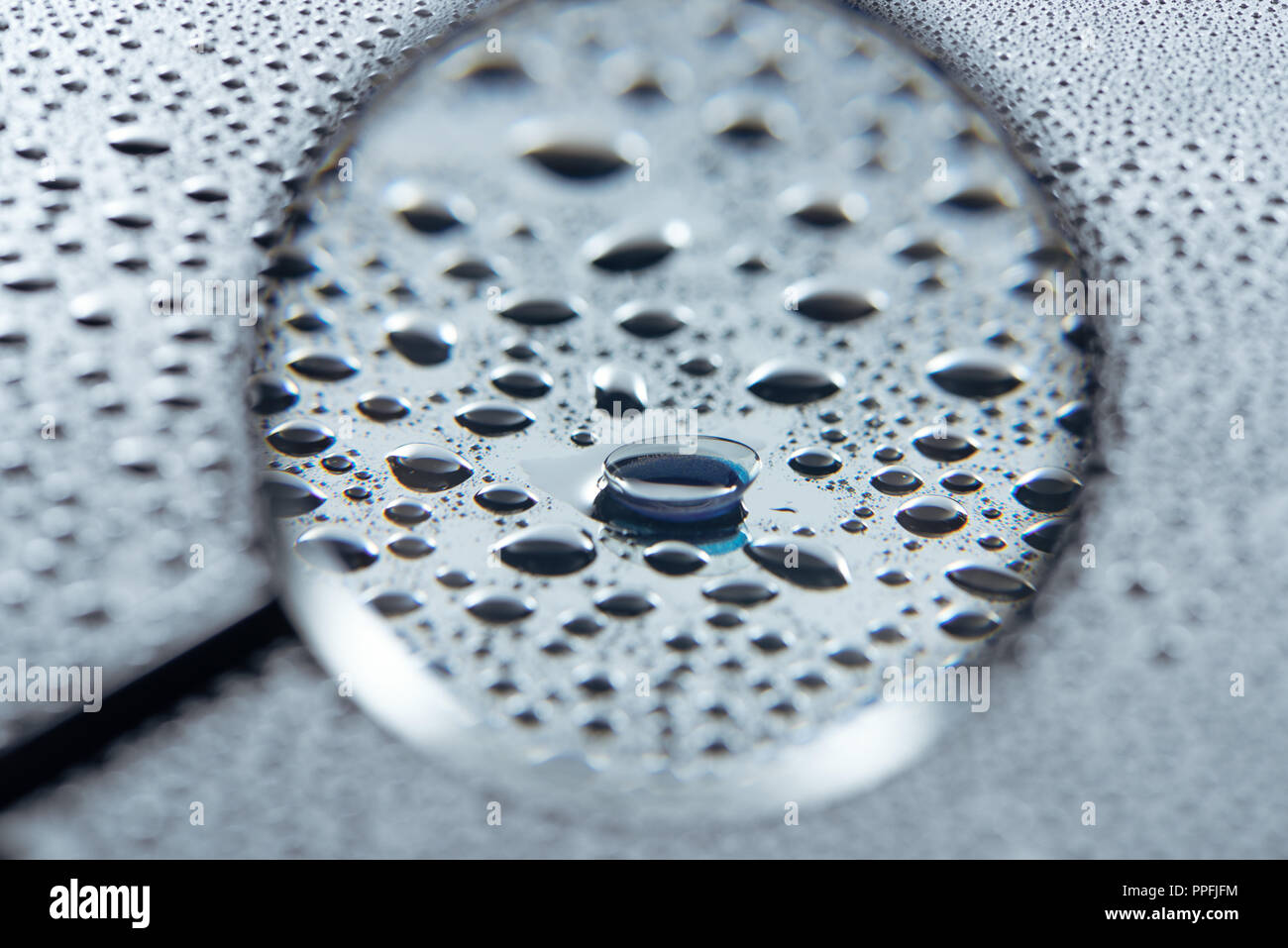 selective focus of magnifying glass and contact lense on grey background with water drops Stock Photo