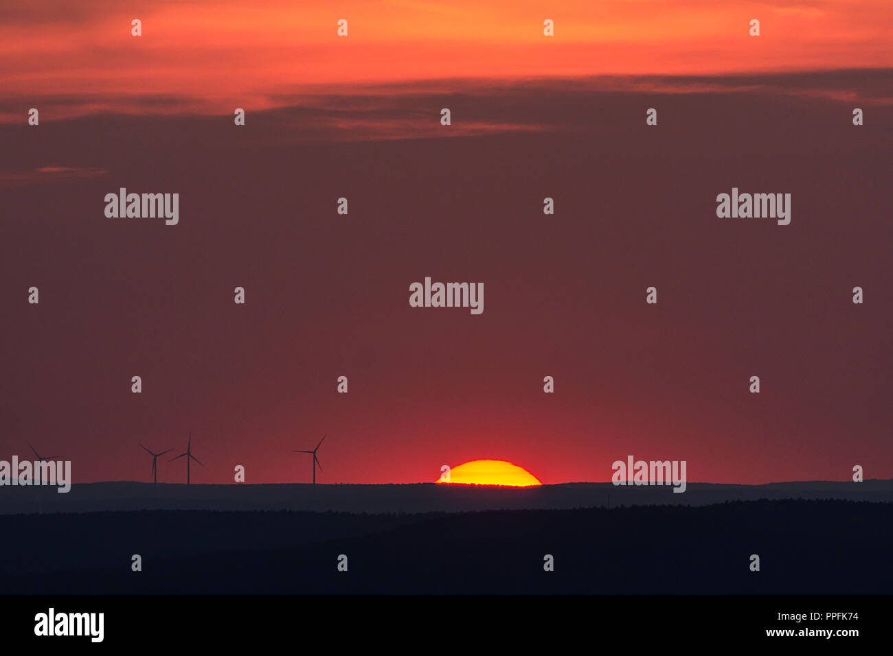 Glowing sun and silhouettes of wind turbines on the horizon, sunset, Bavaria, Germany Stock Photo