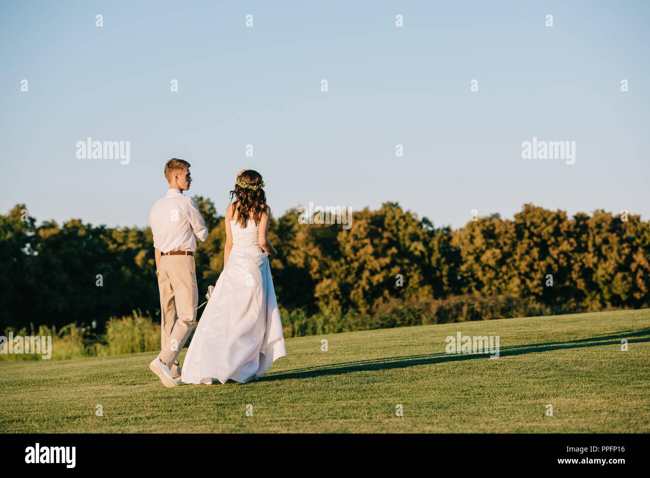 back view of beautiful young wedding couple walking together in park ...