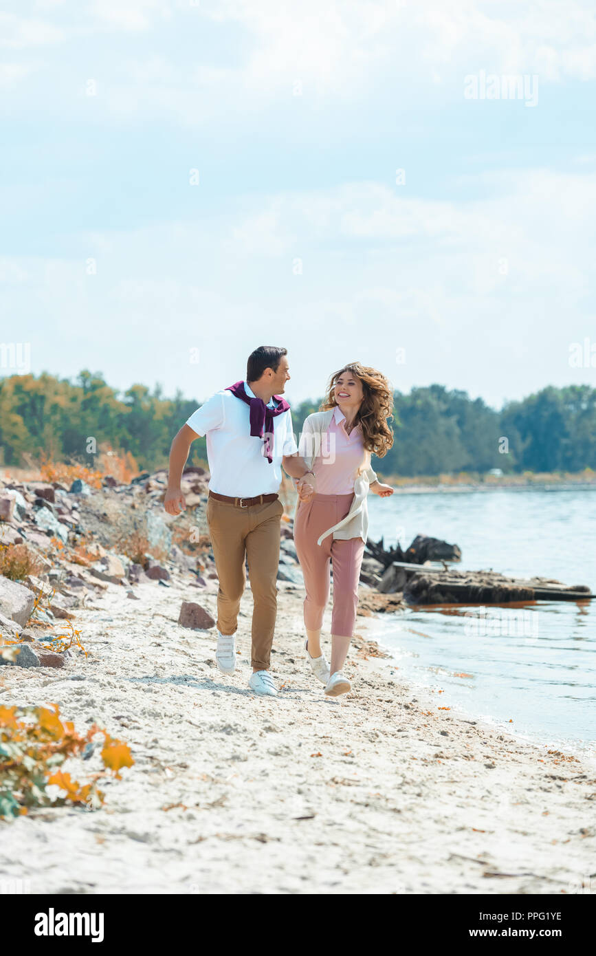 happy couple holding hands while running on sandy beach Stock Photo - Alamy
