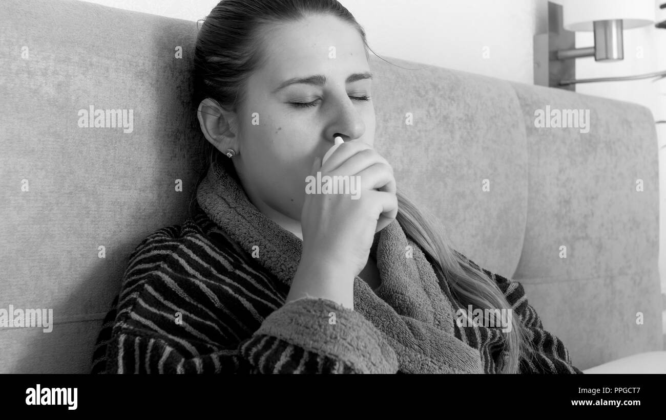 Black and white portrait of sick woman sitting in bed and using nasal spray Stock Photo