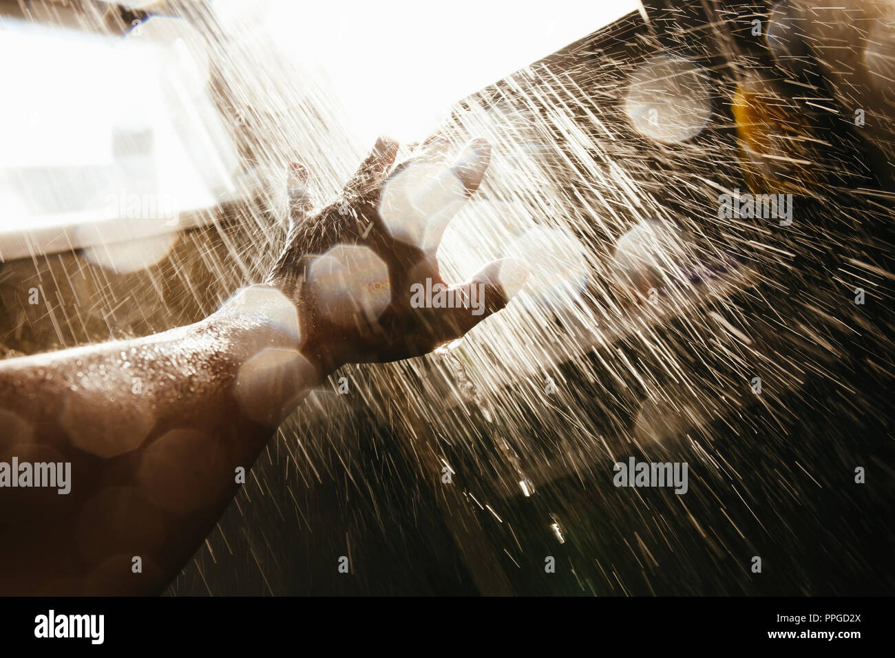 A man's hand in a spray of water in the sunlight against a dark background. Water as a symbol of purity and life. Stock Photo