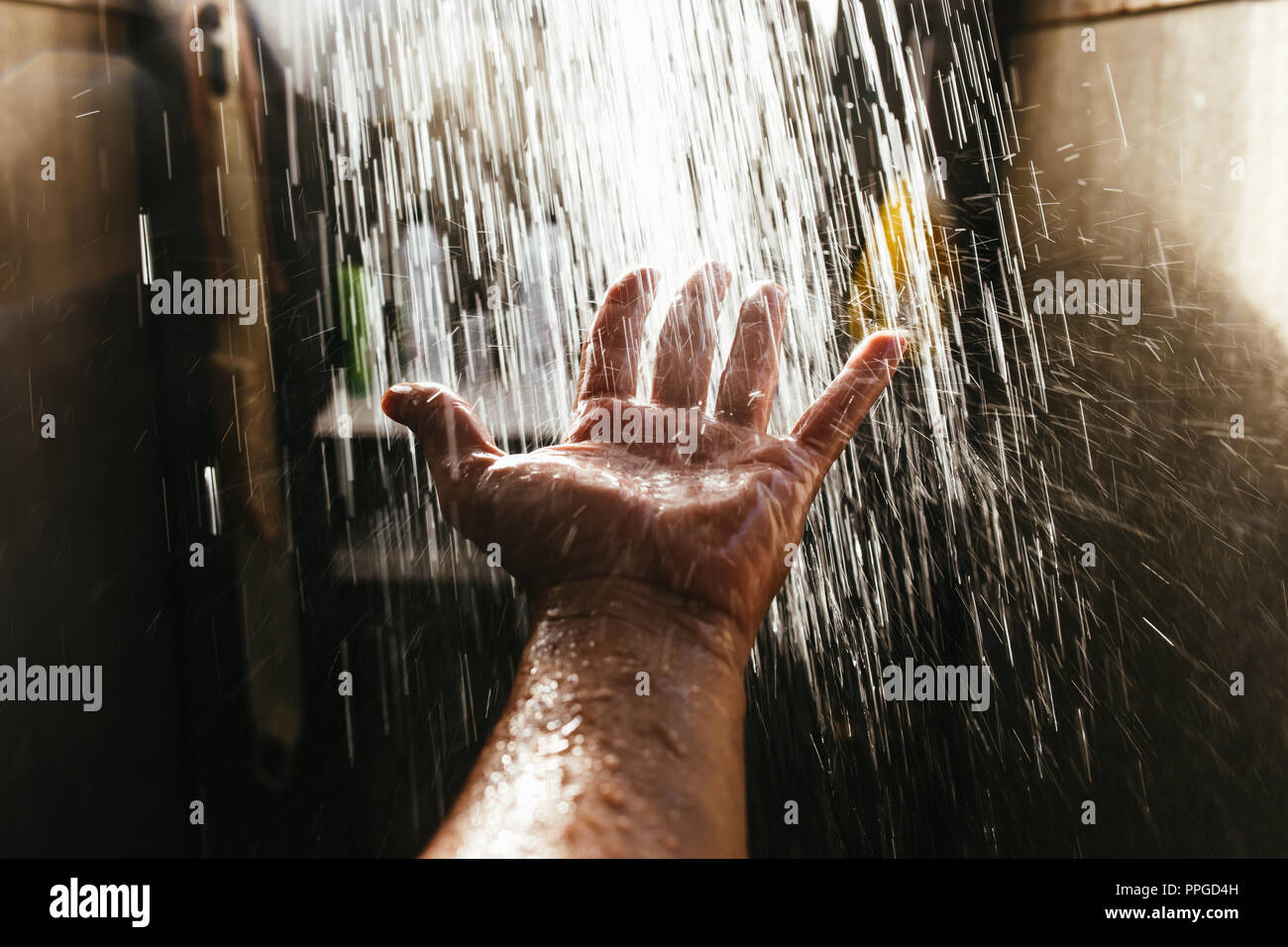 A man's hand in a spray of water in the sunlight against a dark background. Water as a symbol of purity and life. Stock Photo