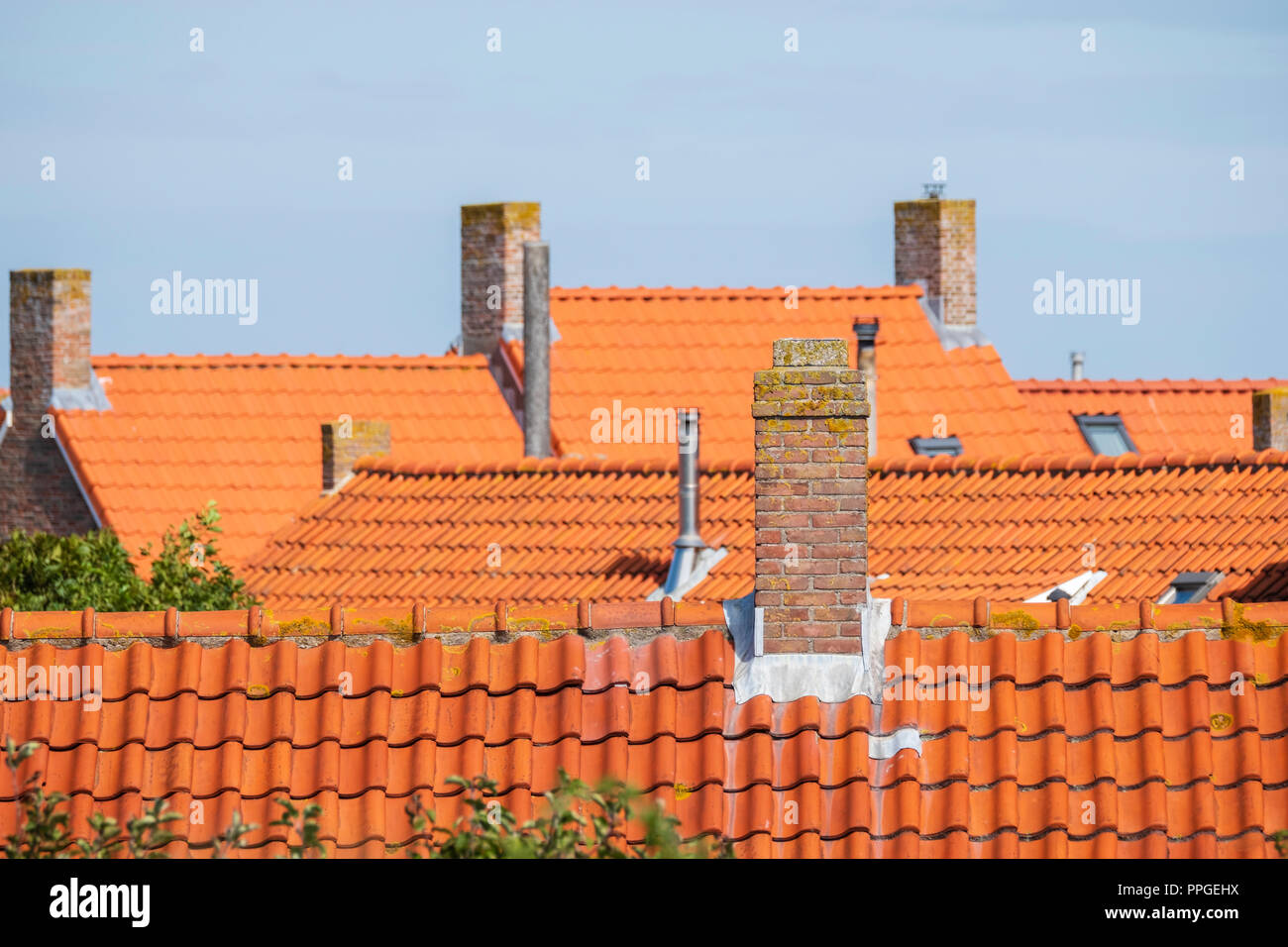 stone chimneys on the roofs with orange roof tiles against a blue sky in an old neighborhood Stock Photo