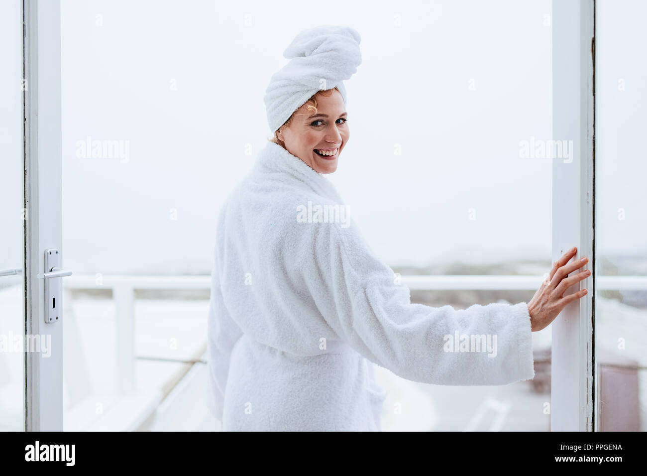 https://c8.alamy.com/comp/PPGENA/smiling-woman-in-a-bathrobe-with-a-towel-wrapped-on-head-rear-view-of-a-woman-standing-in-balcony-after-her-bath-PPGENA.jpg