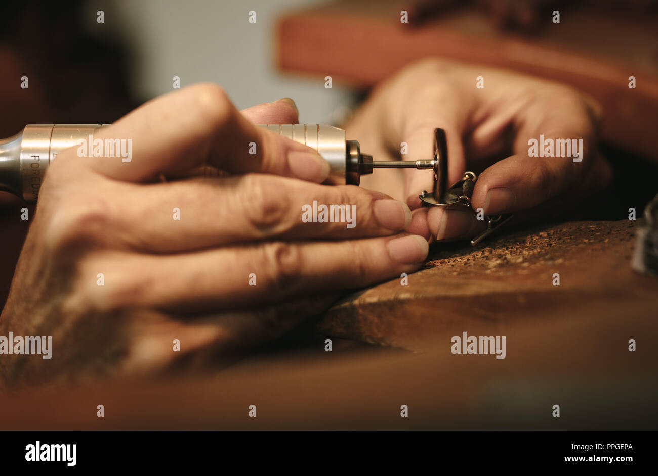 Hands of female jeweler polishing a jewelry piece with grinder machine. Goldsmith making a piece of jewelry at her workbench. Stock Photo