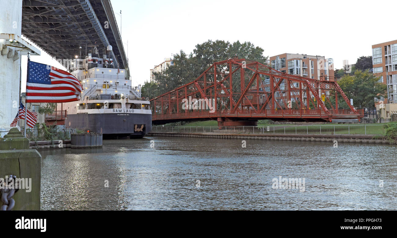 The M/V Sam Laud lake freighter passes the opened red Center Street  swing bridge along the banks of the Cuyahoga River in Cleveland, Ohio, USA. Stock Photo
