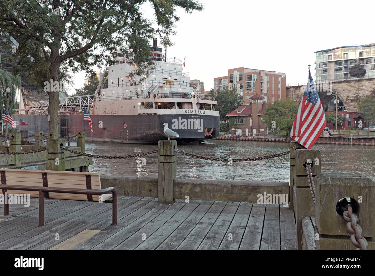A bench in Heritage Park on the banks of the Cuyahoga River offers a view of water vessel traffic, like the M/V Sam Laud, in Cleveland, Ohio, USA. Stock Photo