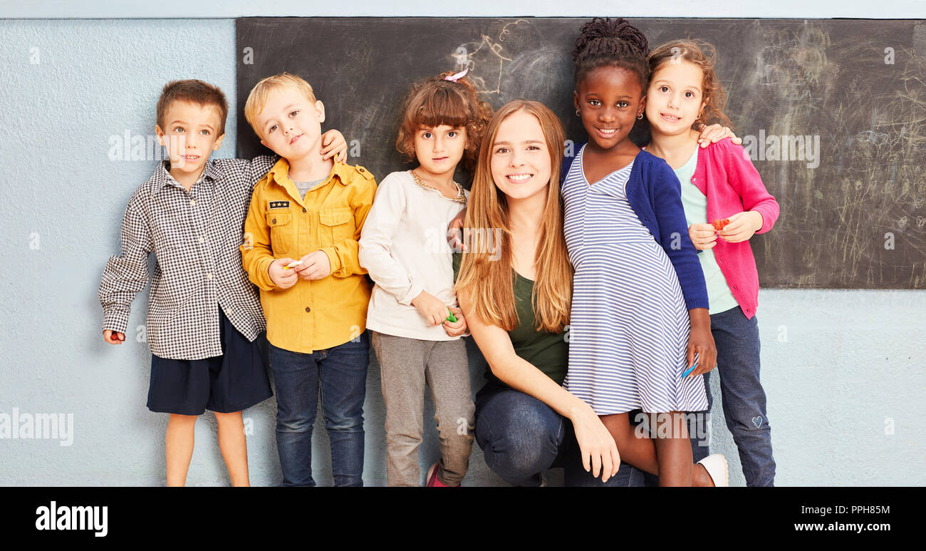 Happy multicultural group of kids with teacher in elementary school in front of a blackboard Stock Photo